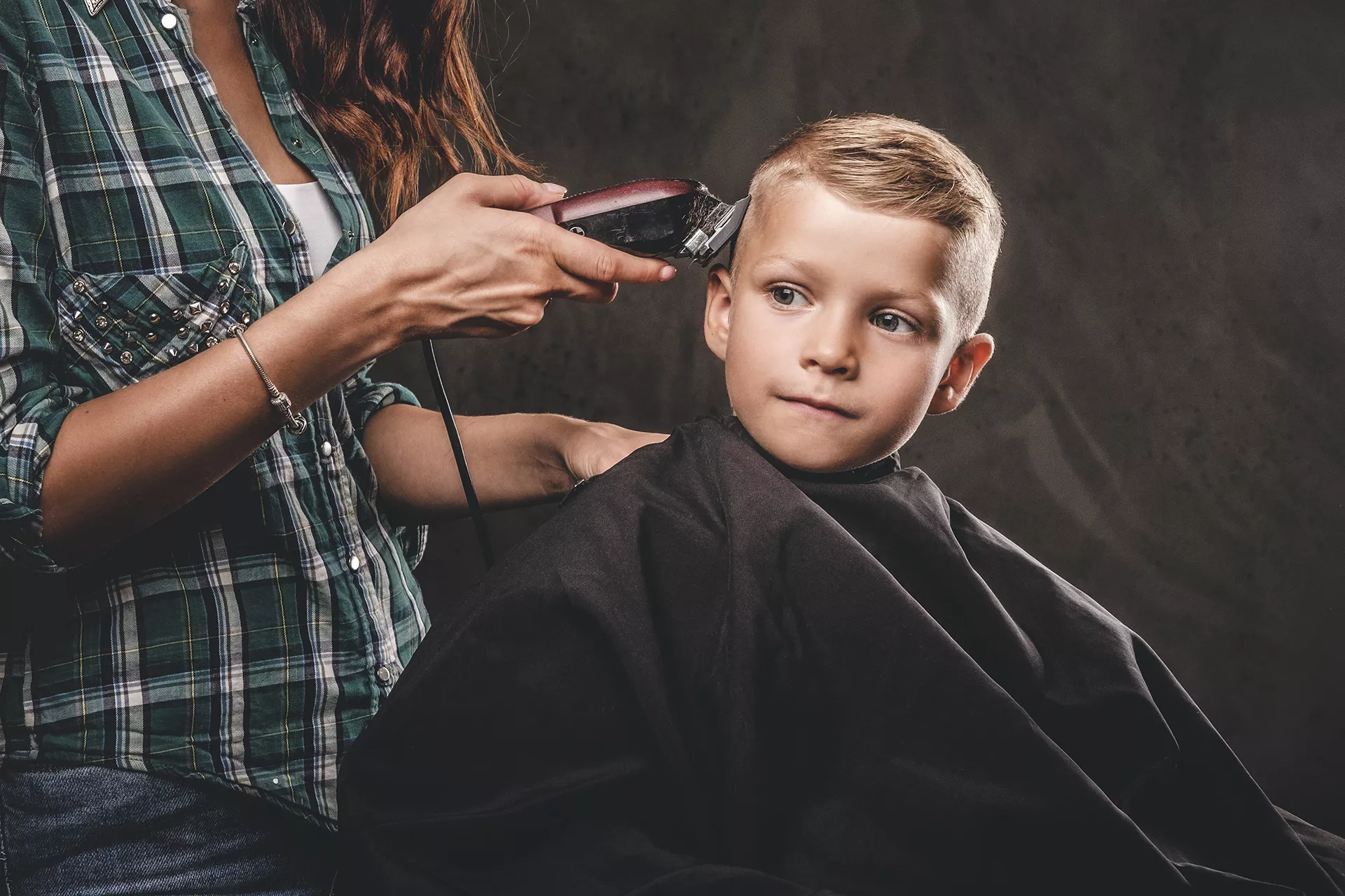 Mujer cortando el pelo a un niño con maquinilla eléctrica
